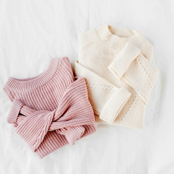 Pale pink and white warm knitted sweaters on bed. Women's stylish autumn or winter clothes. Flat lay, top view.